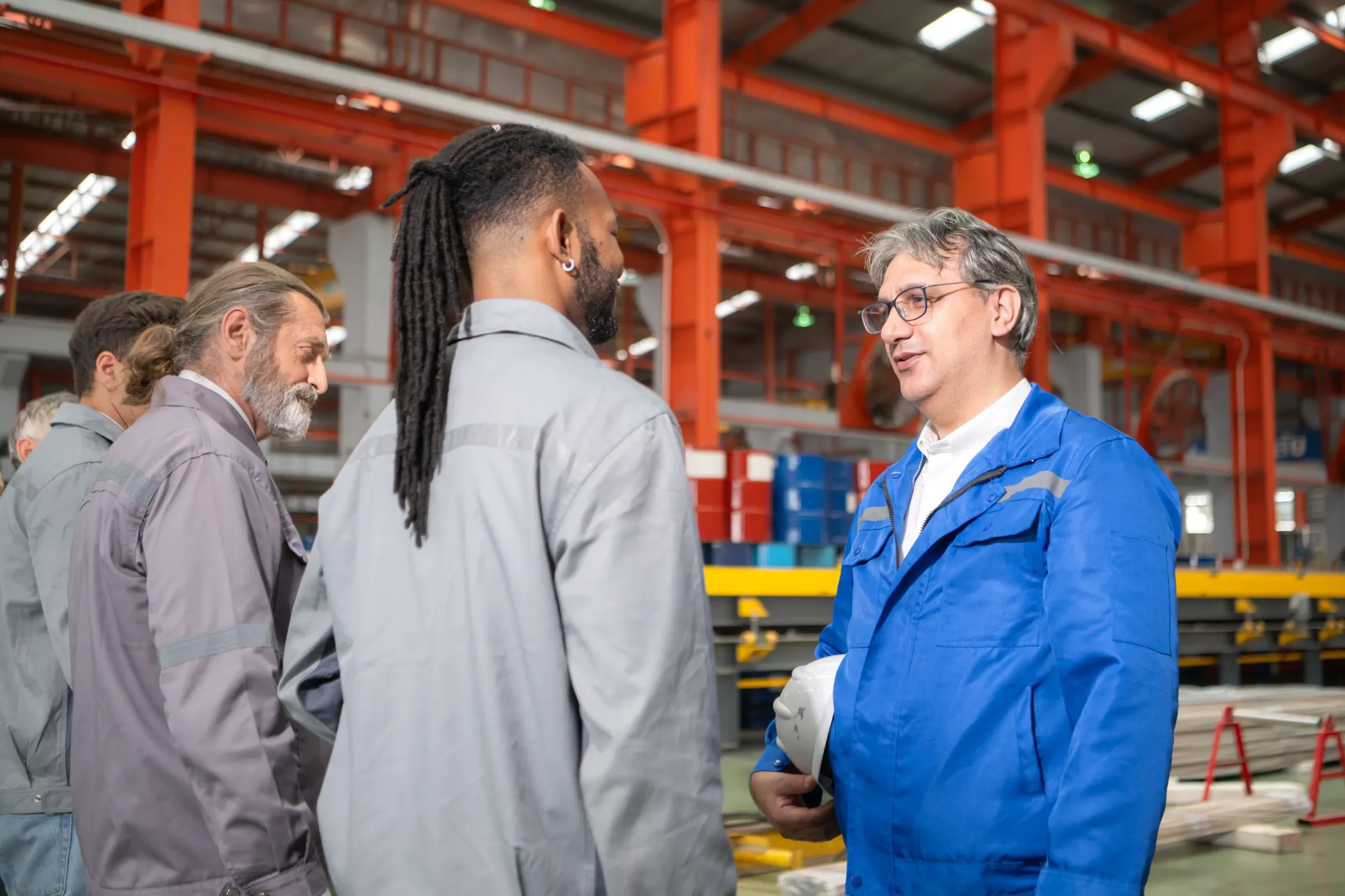 Une équipe en tenue de travail échange debout dans un hall de production.