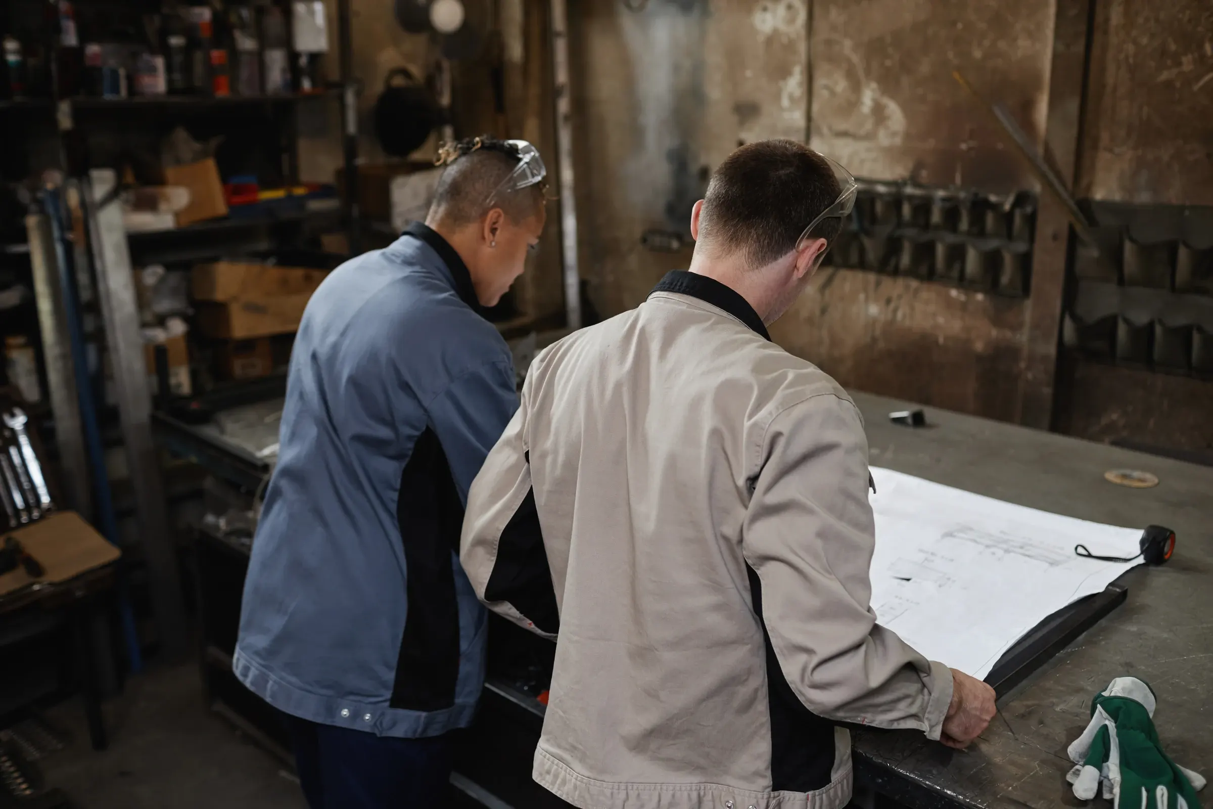 Deux personnes penchées sur des plans dépliés sur un établi d'atelier.